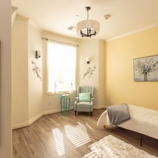 A cozy bedroom with a sunny window, featuring a comfortable chair, bed, and tasteful decor.