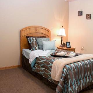 A cozy bedroom featuring a single bed with a wooden headboard, accented by decorative pillows and soft lighting from a bedside lamp.