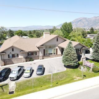 Aerial view of a large house with multiple cars parked in the driveway, surrounded by trees and mountains in the background.
