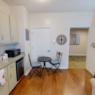 A small kitchen area with a table and two chairs, featuring wooden flooring and cabinets.