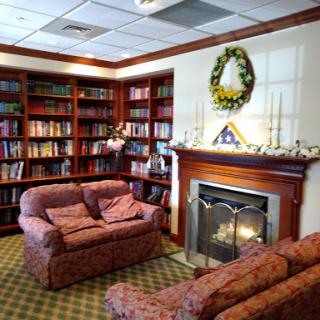 A cozy library space featuring comfortable seating, bookshelves filled with books, and a warm fireplace.