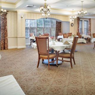 A spacious dining room with elegantly set tables and chairs, featuring chandeliers and large windows.