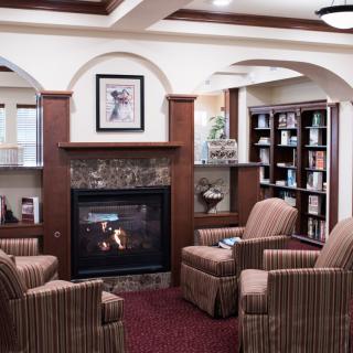 A cozy library with comfortable armchairs around a fireplace and bookshelves lining the walls.