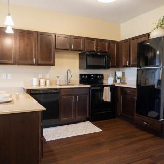 A modern kitchen with dark wooden cabinets, black appliances, and wood flooring.