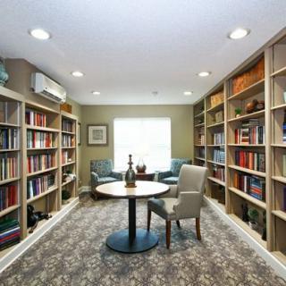 A cozy library with bookshelves lining the walls and a central table with chairs, creating an inviting reading space.