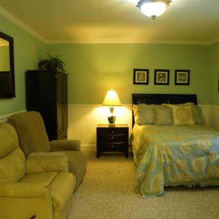 A cozy bedroom with a bed, armchair, nightstand, lamp, and wall decorations.
