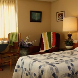 A cozy bedroom with a decorated bed, chairs by the window, and a lamp on the nightstand.