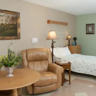 A cozy room with a bed, armchair, and table, decorated with lamps and artwork.