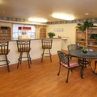 A cozy indoor space with a kitchen counter and bar stools, featuring wood flooring and decorated with shelves and plants.