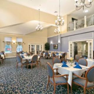 A spacious dining area with neatly arranged tables and chairs, elegant chandeliers, and a patterned carpet.
