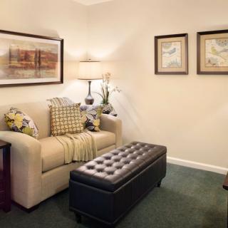 A cozy living room with a beige couch, artwork on the walls, and a tufted leather ottoman.