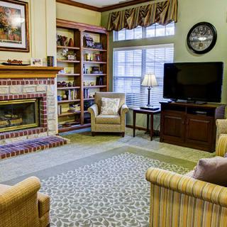A cozy living room featuring a fireplace, bookshelves, armchairs, and a television.