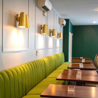A modern restaurant interior with green upholstered seating, wooden tables, and stylish wall lighting.