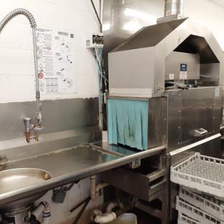 A view of a commercial kitchen cleaning area featuring a dishwasher and stainless steel sink.