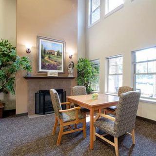 A cozy living room with a fireplace, table, and chairs surrounded by decor and large windows.