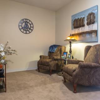 A cozy living room with two armchairs, a lamp, wall art, and a decorative clock.