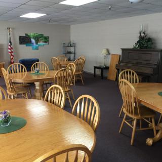A community meeting room with wooden tables and chairs, featuring a piano and an American flag.