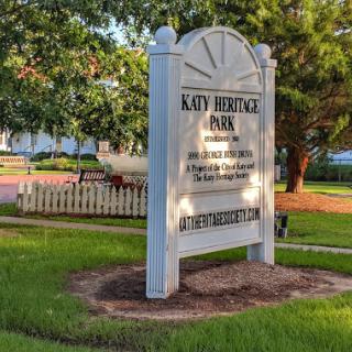 A historic sign marking a point of interest in Katy, Texas, surrounded by lush greenery.