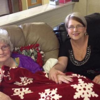 Two women sitting together on a couch, covered with a festive blanket.