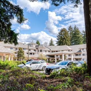 A scenic view of a building surrounded by trees with cars parked in front under a blue sky with clouds.