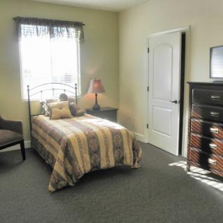 A cozy and well-lit bedroom featuring a single bed, dresser, and comfortable seating.