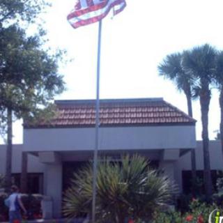 A view of a building with an American flag flying in front, surrounded by palm trees.