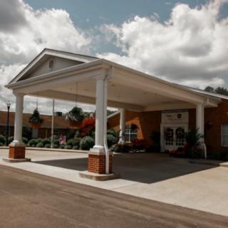 A building entrance with large columns and a driveway under a cloudy sky.
