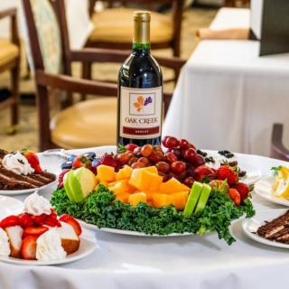A table set with a bottle of wine, a fruit platter, and assorted desserts.