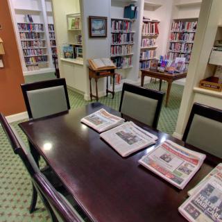A cozy library reading area with newspapers on a table surrounded by bookshelves.