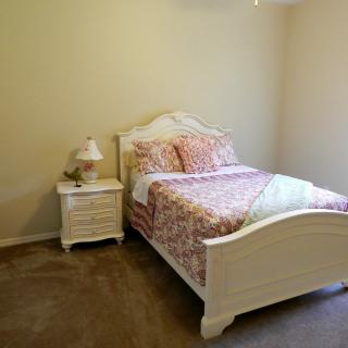 A cozy bedroom with a white bed, floral bedding, and a matching nightstand with a lamp.