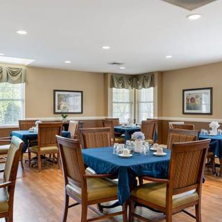 A cozy dining room with neatly arranged tables and chairs, featuring wooden flooring and warm decor.
