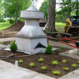 A stone monument surrounded by newly planted landscaping in an outdoor setting.