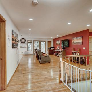 A spacious living room featuring hardwood floors, comfortable seating, a television, and a red accent wall, with a view of the staircase.
