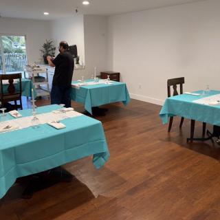 A dining area with several tables covered in turquoise tablecloths, set in a room with wooden floors.