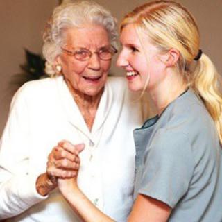 A caregiver dances with an elderly woman, both smiling and enjoying the moment.