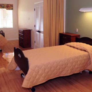 A simple nursing home bedroom with two beds and wooden flooring.