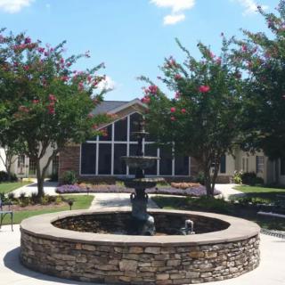 A courtyard featuring a stone fountain surrounded by trees and a building in the background.