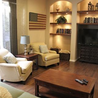 A cozy living room with armchairs and a wooden coffee table, featuring shelves with books and a flag decoration.