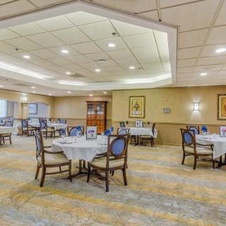 An elegant dining room with neatly arranged tables and chairs, featuring bright lighting and a carpeted floor.