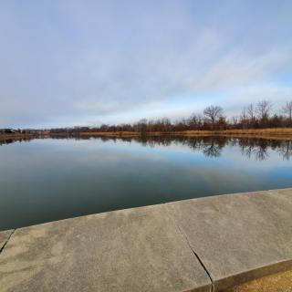 A serene view of a calm lake reflecting the sky and surrounding trees.