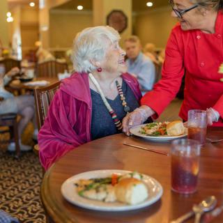An elderly woman is being served a meal by a server in a restaurant setting.
