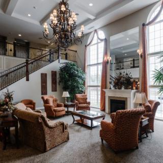 A luxurious living room with elegant furniture, a grand chandelier, and a prominent staircase.