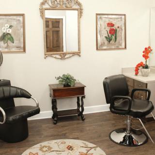 A cozy hair salon interior featuring stylish chairs, a large mirror, and floral decor.
