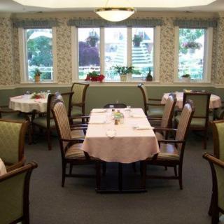 A cozy dining room with neatly set tables and chairs, featuring large windows.