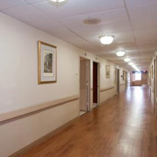 A long indoor hallway with a wooden floor and ceiling lights, adorned with framed pictures on the walls.