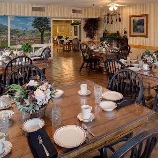 A cozy dining room setup with wooden tables, elegant table settings, and decorative flowers.