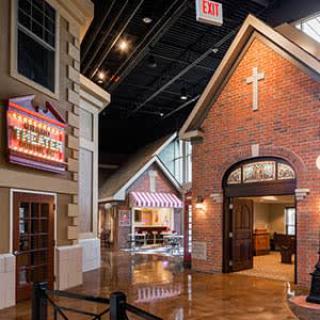 A cozy indoor setting featuring a brick church, a theater sign, and storefronts under high ceilings.