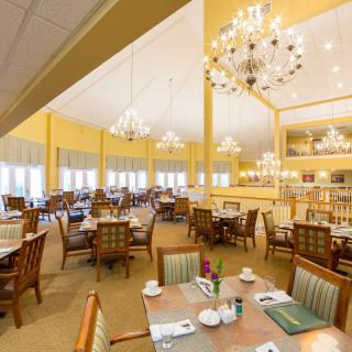 An elegant dining room with chandeliers, decorated in a warm color palette, featuring neatly arranged tables and chairs.