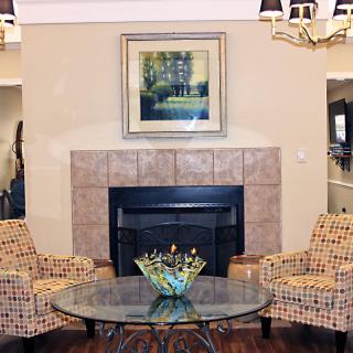 A cozy living room features a central fireplace, flanked by patterned chairs and a glass coffee table topped with decorative items.