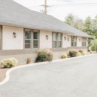 A single-story building with multiple windows, surrounded by shrubs and a paved road.